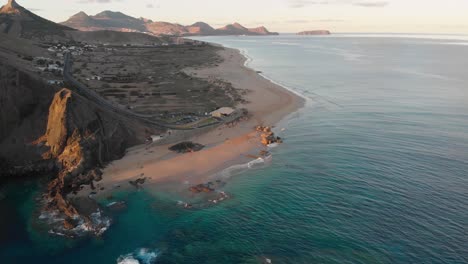 Sensational-summertime-dramatic-flight-approaching-beautiful-sandy-beach-of-Calheta-with-waves-rolling-on-shoreline-coast-at-sunset,-Madeira,-Portugal,-overhead-aerial-descend