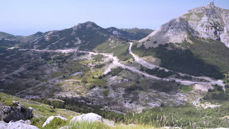 Eine-Spektakuläre-Aussicht-Vom-Njegos-Mausoleum,-Dem-Berg-Lovcen-In-Montenegro,-Mit-Weiten-Grünen-Tälern-Zwischen-Scharfen-Bergkämmen,-Kleinem-Kiefernbusch-Auf-Der-Linken-Seite,-Straßen-Und-Bäumen-Unten,-Schwenk-In-4K-Aufnahme