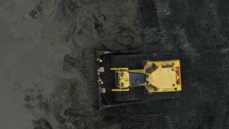 Top-down-rising-aerial-view-of-a-bulldozer-moving-mud-on-a-construction-site