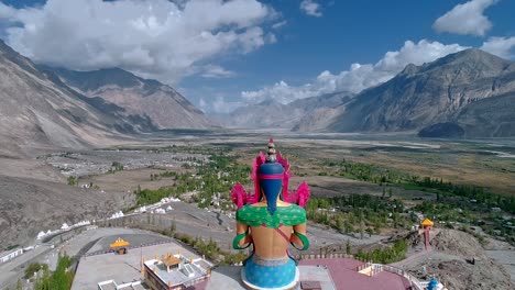 aerial-back-view-of-a-tall-lord-Budha-statue-facing-towards-a-majestic-mountain-valley