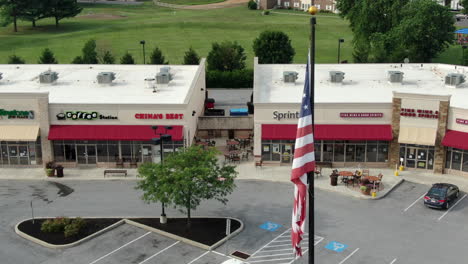 Strip-mall-under-American-flag,-brick-and-mortar-retailers-struggle,-going-out-of-business,-bankruptcy-as-consumers-shift-to-online-shopping