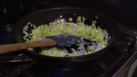 Seasoning-leek-and-onion-in-frying-pan-with-resting-spatula,-indoor-cooking
