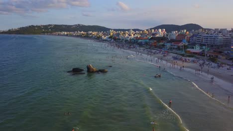 Aerial-view-of-tourists-bathing-and-swimming-on-the-sea-in-Bombas-Beach-at-golden-hour