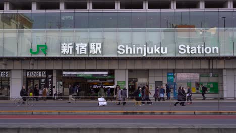 Vorderansicht-Des-Bahnhofs-Shinjuku-Mit-Auto-Und-Einheimischen,-Die-Tagsüber-Die-Straße-Passieren-–-Totalaufnahme