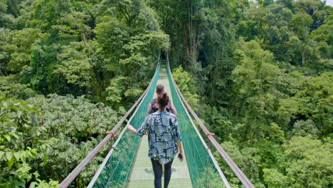 Cámara-Lenta-De-Un-Par-De-Turistas-Caminando-Por-Un-Puente-Colgante-En-Medio-De-La-Selva-Tropical-En-Arenal,-Costa-Rica