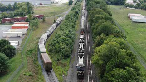 Diesel-locomotive-engine-train-on-track,-loading-and-unloading-at-transportation-distribution-center-buildings,-orbiting-aerial-shot,-rail-and-ground-transit-shipping-theme