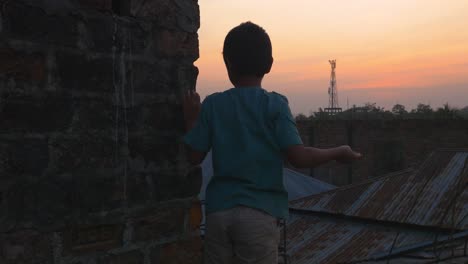 Kleiner-Junge-Wirft-Steine-Vom-Dach-In-Sylhet-Bei-Sonnenuntergang,-Bangladesch