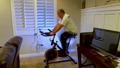 Zeitraffer-Eines-Reifen-Mannes,-Der-Zu-Hause-Auf-Einem-Stationären-Fahrrad-Trainiert,-Sich-Aufwärmt,-Cardio-Macht-Und-Auf-Einem-Tablet-Liest-–-Langzeitbelichtung,-Bewegungsunschärfe