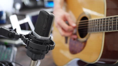 A-studio-musician-playing-an-acoustic-guitar-and-recording-audio-into-a-condenser-microphone