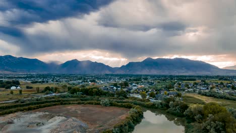 Clouds-gather-across-the-valley-mountains-as-sunshine-rays-burst-through-and-the-sky-reflects-off-the-water---aerial-hyperlapse