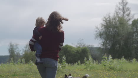 Slow-motion-shot-of-sunlit-mother-and-child-walking-with-dog-in-meadow