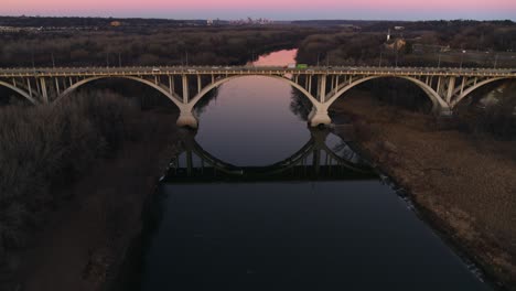 Ascending-symmetrical-view-of-Mendota-Bridge,-over-Minnesota-River,-in-front-of-a-pink-evening-sky