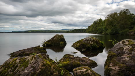 Zeitraffer-Eines-Sees-Mit-Großen-Felsen-Im-Vordergrund-Und-Wald-In-Der-Ferne-An-Einem-Bewölkten-Sommertag-In-Der-Ländlichen-Landschaft-Irlands