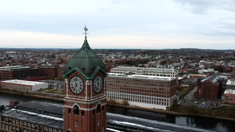 Close-Up-View-Of-Ayer-Mill-Clock-Tower-With-Commercial-And-Industrial-Buildings-Along-Merrimack-River-In-The-Background-In-Lawrence,-Massachusetts