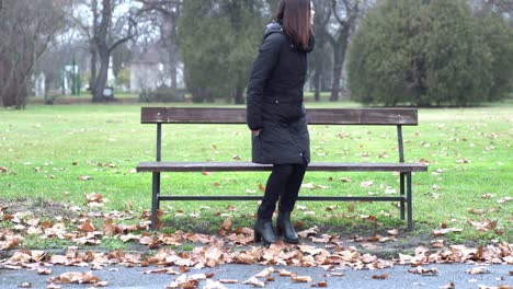 Young-woman-walking-in-a-park-and-sitting-alone-on-a-bench-on-a-cold-day