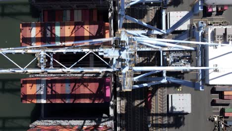 Mesmerizing-lines-and-multicolored-shipping-containers-being-unloaded,-aerial-god-view