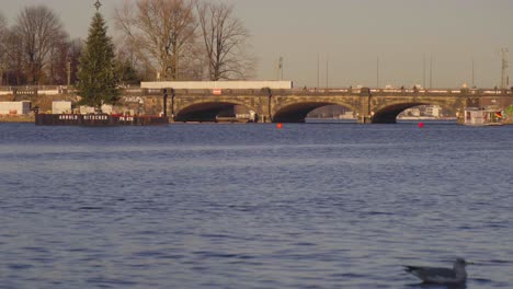 Vista-Del-Puente-Lombardsbrücke-En-Hamburgo,-Alemania,-A-Través-Del-Lago-Alster-Interior-Con-Un-Tren-Moviéndose-Y-Un-árbol-De-Navidad-En-Primer-Plano