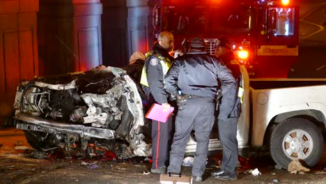 Three-police-officers-talking-in-front-of-car-wreck-as-firefighter-steps-into-fire-engine-in-the-background