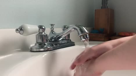 Child-washes-their-hands-in-a-white-sink