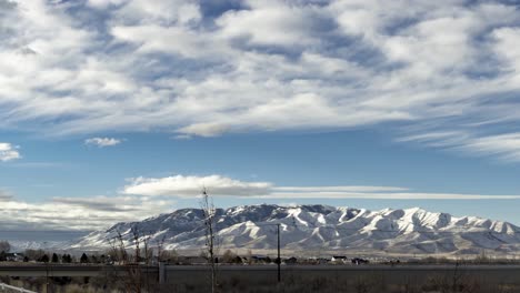 A-busy-highway-in-the-foreground-with-a-snowy-mountain-in-the-background-and-cloudscape-overhead---panning-time-lapse