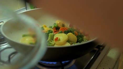 Cooking-and-mixing-frozen-vegetables-in-a-white-frying-pan,-making-healthy-vegetarian-food,-steam-coming-up,-closeup-handheld-shot