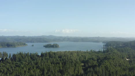 Slowly-ascending-drone-shot-of-lush-Oregon-coast-forest-and-blue-lake