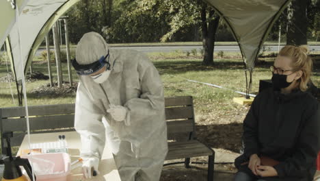 Person-in-PPE-takes-COVID-sample-from-woman-in-mask-at-outdoor-testing-site