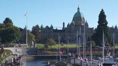 4K-slow-motion-shot-of-the-British-Columbia-parliament-and-the-Victoria-harbour-with-boats-and-people-walking-around-on-a-beautiful,-sunny-day