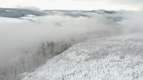 Aerial-dolly-out-snowy-landscape-hills-pine-trees-fog-clouds-valley