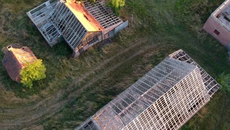 Sliding-overhead-of-run-down-farm-buildings-at-sunset,-no-roof