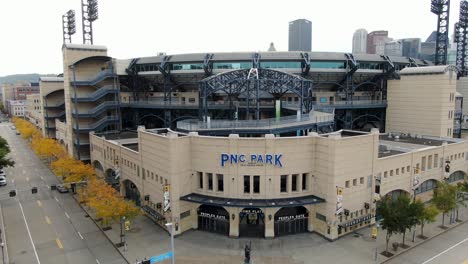Aerial-tilt-up-reveals-front-entrance-of-PNC-Park,-home-of-Pittsburgh-Pirates-MLB-major-league-baseball-team,-yellow-autumn-foliage