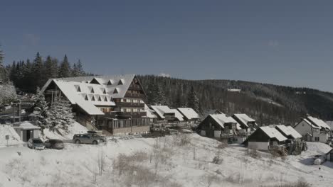 Lukov-Dom-hotel-and-cabins-at-the-Kope-winter-sport-resort-with-a-blackbird-flying,-Aerial-pan-right-shot