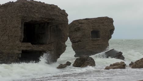 Big-stormy-waves-breaking-against-abandoned-seaside-fortification-building-ruins-at-Karosta-Northern-Forts-in-Liepaja,-Baltic-sea-coastline,-wave-splash,-overcast-day,-medium-shot