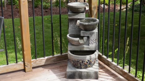 At-the-corner-of-a-wooden-deck,-water-starts-pouring-from-the-top-basin-of-a-fountain-into-subsequent-levels-from-a-recirculating-pump