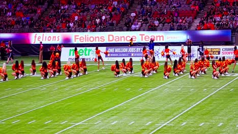 BC-Stadium-Lions-Felions-Cheerleaders-start-jump-dance-cheer-routine-on-indoor-artificial-green-grass-turf-the-other-side-of-the-field-during-footbal-game-side-change-break-with-happy-fans-cheering