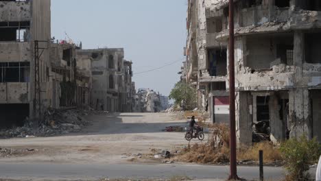 Still-shot,-a-motorcycle-going-behind-the-ruined-buildings-in-the-city-of-Homs-in-Syria