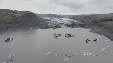 Aerial-drone-view-over-a-lagoon,-towards-the-Solheimajokull-Glacier,-in-cloudy-Iceland