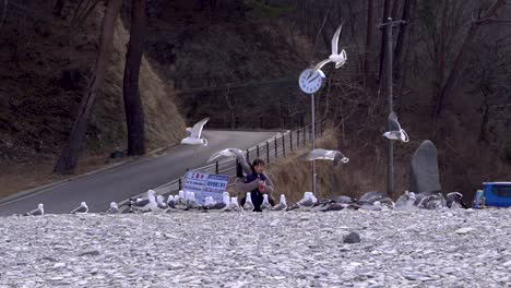 Asian-mother-and-daughter-feeding-seagulls-on-beach-while-laughing