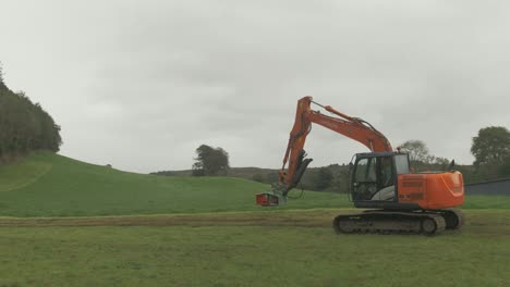 Tree-shear-attachment-on-digger-excavator-enters-field-driving-towards-forestry-edge