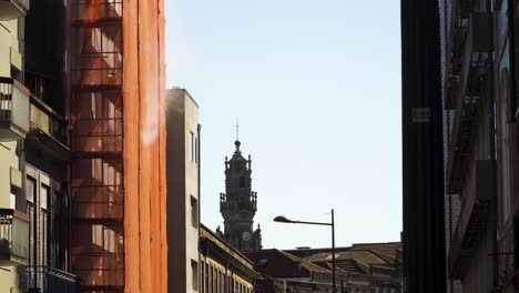 4K-Bau-Eines-Gebäudes-Mitten-In-Der-Stadt-Porto-Mit-Dem-Kirchenturm-Im-Hintergrund,-Etwas-Staub-Dringt-Aus-Den-Fassadenschutzvorrichtungen