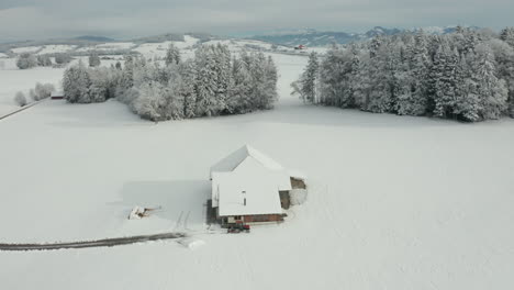 Jib-down-of-small-farmhouse-standing-in-snow-covered-landscape