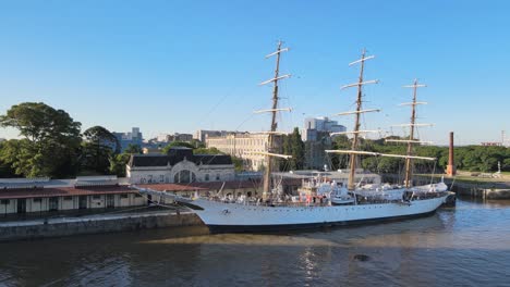 Aerial-pan-left-of-famous-ARA-Libertad-sailing-ship-docked-in-Puerto-Madero-pier-at-daytime,-Buenos-Aires