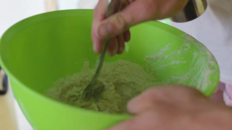 Mixing-flour-with-water-using-a-spoon-in-a-green-bowl-to-make-a-dough-for-baking