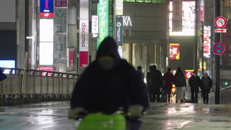 Anciano-Corriendo-En-Una-Carretera-Asfaltada-Mojada-Con-Gente-En-Las-Luces-De-La-Calle-Nocturna-En-La-Ciudad-De-Shunjuku,-Tokio,-Japón