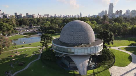Aerial-pan-right-of-Galileo-Galilei-Planetarium-in-Palermo-Woods-with-buildings-in-background-at-daytime,-Buenos-Aires