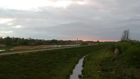 Fliegende-Drohne-über-Dem-Nächsten-Sumpfgebiet-Der-Kirchenstadt-Bei-Sonnenuntergang,-Aufsteigend