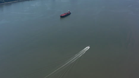 A-drone-view-of-a-large-red-barge-anchored-and-a-small-boat-going-by-in-the-Hudson-River-in-NY-on-a-sunny-day