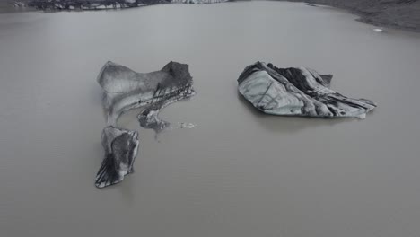 Aerial-view-over-blackned-ice-blocks-on-the-Solheimajokull-glacier-lagoon---tilt,-drone-shot