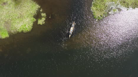 Drone-shot-of-a-canoe-paddling-into-a-small-channel-with-sunlight-reflections