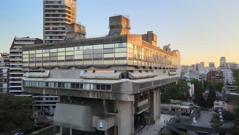 Aerial-dolly-out-of-modern-exposed-concrete-National-Library-between-buildings-at-golden-hour,-Buenos-Aires
